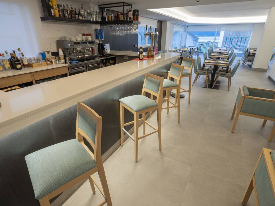 A modern bar area with a long counter, bar stools, and a variety of liquor bottles.