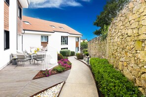 A modern house with a stone wall, a paved patio, and a garden with flowers. - Hotel Meiga do Mar & Spa (Carnota)
