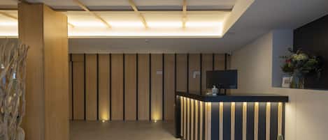 Un área de recepción moderna con un panel de pared de madera, un mostrador de recepción con tiras de luz verticales y un televisor de pantalla plana.