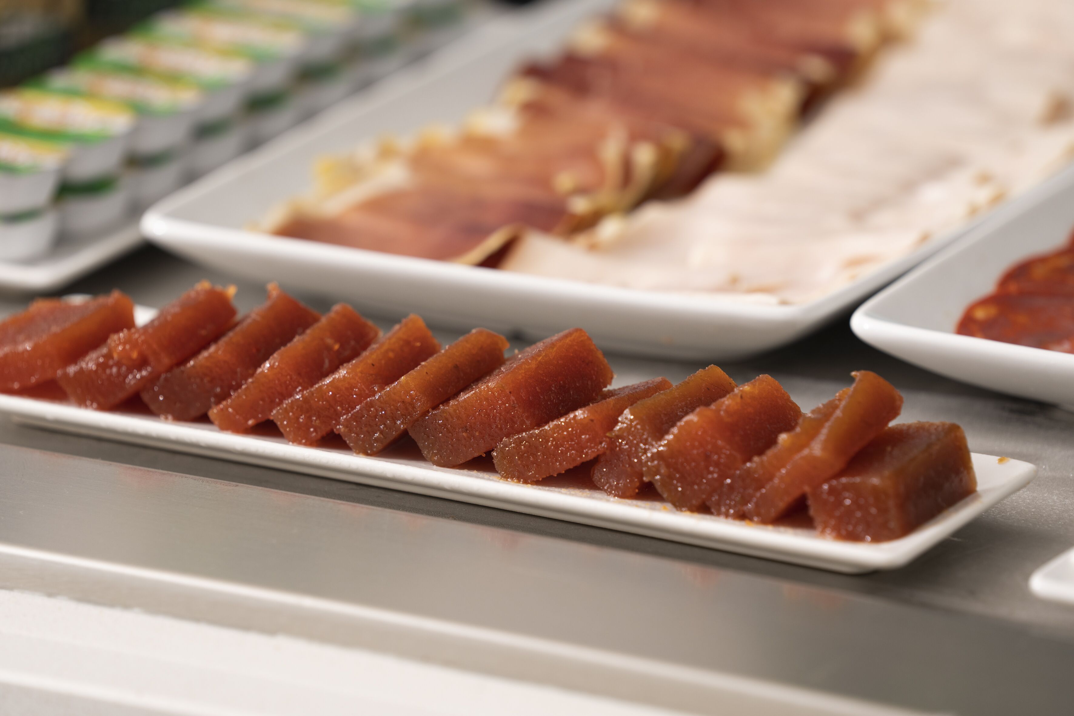 Un bufé con diversas opciones de comida, incluyendo un plato con carne en cubos y una fuente con un postre glaseado.