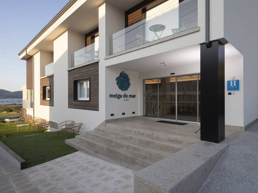 Um hotel moderno com entrada de vidro, área de estar externa e vista para o mar.
