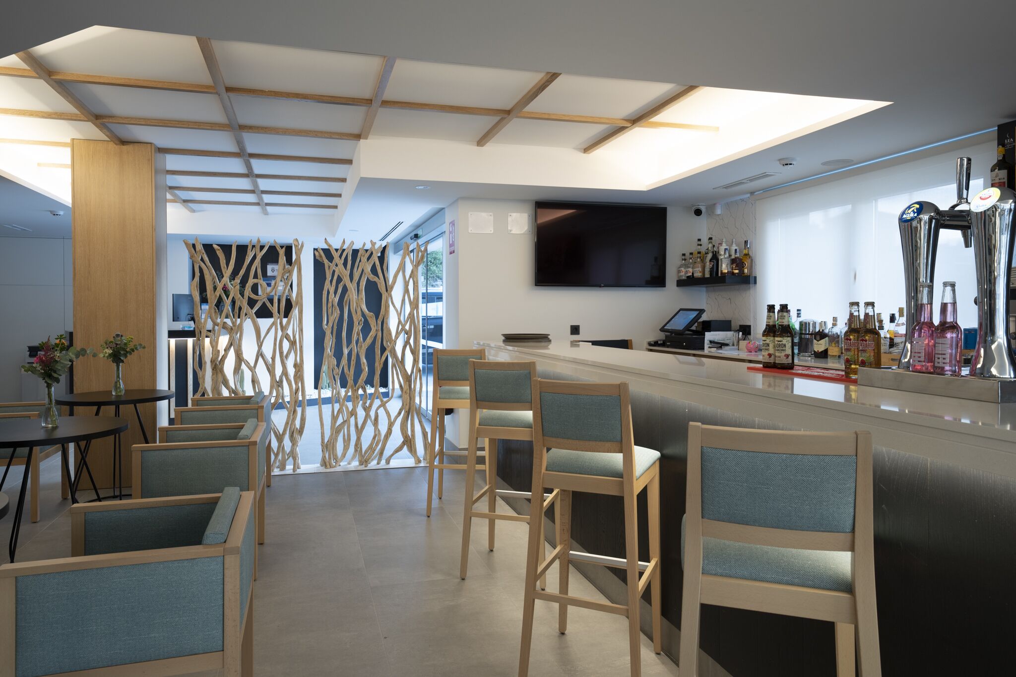 Un área de bar moderna con sillas de madera, una barra y un televisor de pantalla plana montado en la pared.