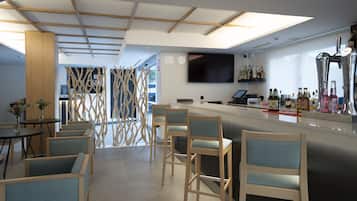 Un área de bar moderna con sillas de madera, una barra y un televisor de pantalla plana montado en la pared.
