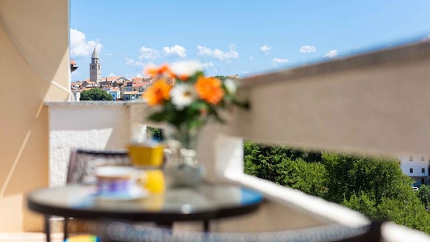 Un balcon avec une table et un vase de fleurs, donnant sur un paysage urbain dominé par une tour imposante.