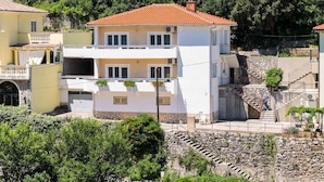 Un bâtiment à deux étages, doté d’un toit recouvert de tuiles rouges, d’un escalier en pierre et d’un balcon.