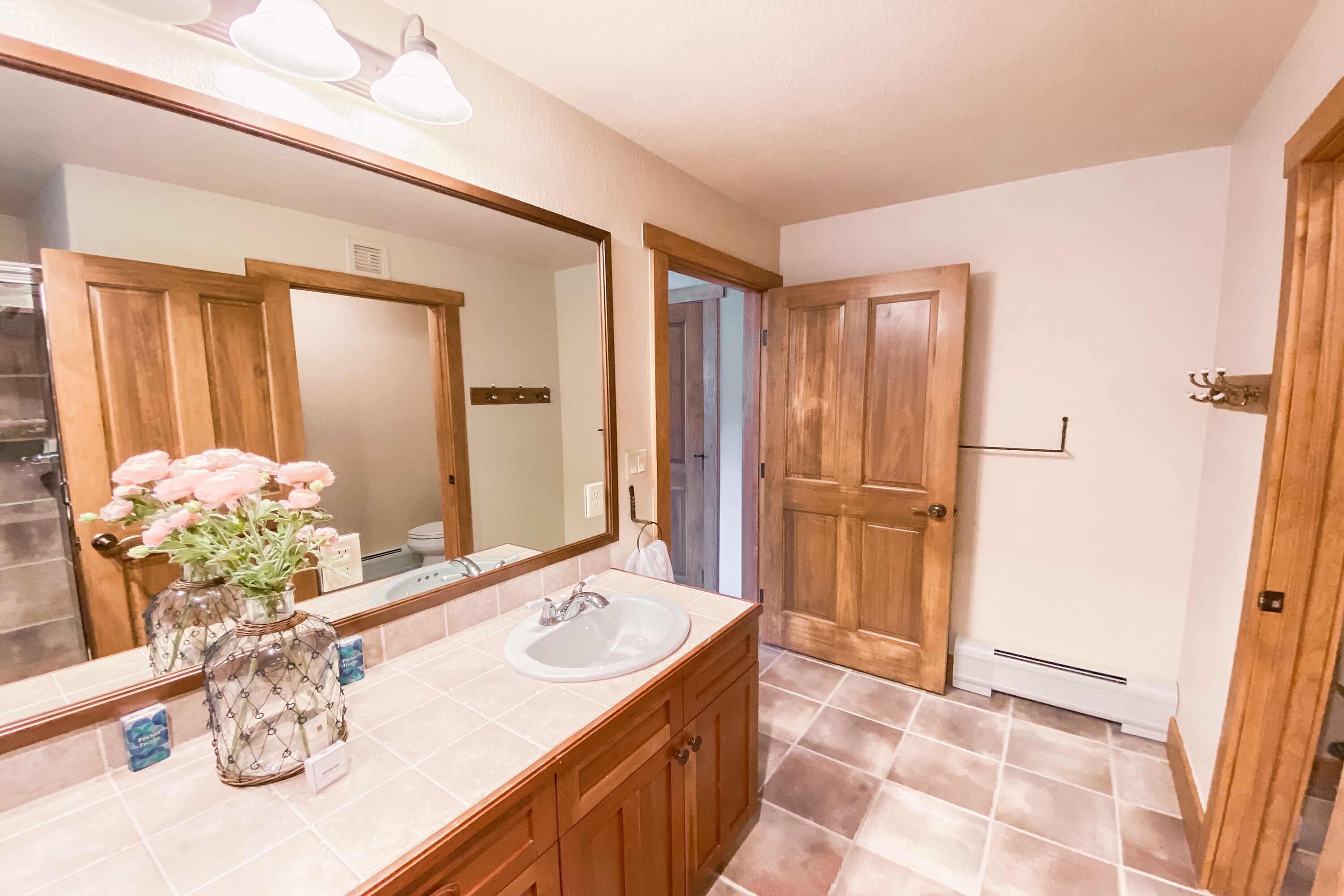 A bathroom with a wooden vanity, a large mirror, and a vase with flowers.