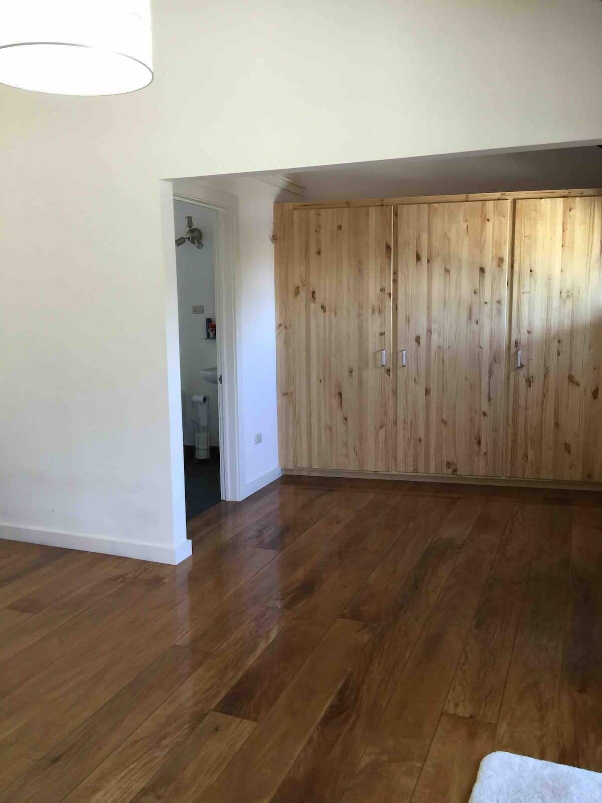 Una stanza con pavimento in legno, un ampio armadio e una porta che conduce a un'altra stanza.