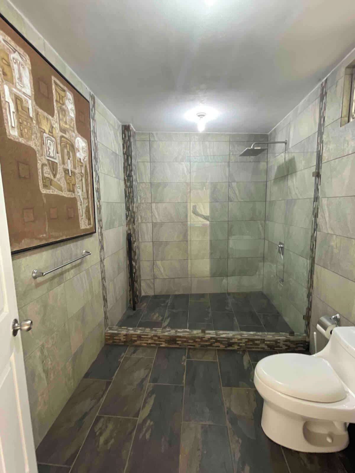 A bathroom with a shower, toilet, and a tiled floor.