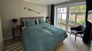 Quarto com uma cama grande, decoração de parede com remo de madeira, uma cadeira e vista para o verde através de uma porta deslizante.