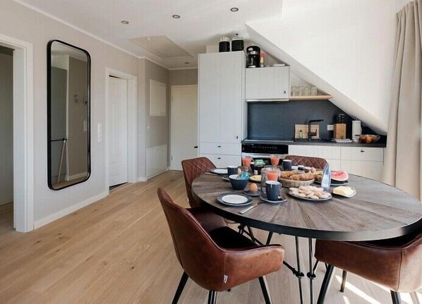 A modern kitchen with a dining area, featuring a round table with chairs, a built-in oven, and a breakfast spread.