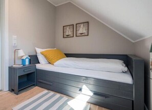 A bedroom with a dark wooden bed, white bedding, a yellow pillow, a nightstand with a lamp, and two sailboat paintings on the wall.