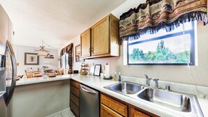 A kitchen with wooden cabinets, a stainless steel sink, and a window with a view of greenery. - Mama Bear's Den by Ruidoso Vacation Rentals (Ruidoso)