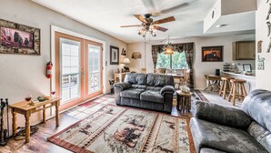 A spacious living room with a fireplace, a ceiling fan, and a dining area with wooden furniture. - Mama Bear's Den by Ruidoso Vacation Rentals (Ruidoso)