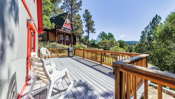 A wooden deck with rocking chairs and a view of a cabin. - Mama Bear's Den by Ruidoso Vacation Rentals (Ruidoso)