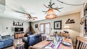 A cozy living room with a fireplace, a dining area with a wooden table and chairs, and a ceiling fan. - Mama Bear's Den by Ruidoso Vacation Rentals (Ruidoso)