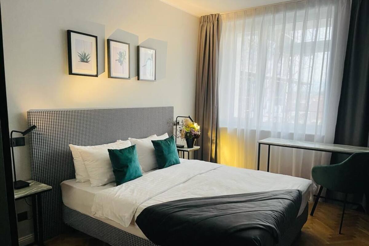 A neatly arranged hotel room with a large bed, a desk, and a chair. There are three framed pictures on the wall.