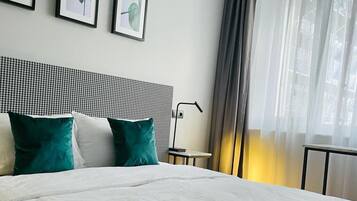 A hotel room with a bed, a headboard, a bedside table, and a window with curtains.