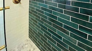 Casa de banho com parede revestida a azulejos brancos e zona de duche com azulejos verdes.