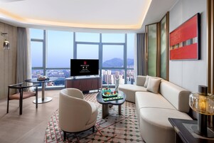 Una habitación de hotel moderna con un ventanal que ofrece vistas a la ciudad, un televisor de pantalla plana, un sofá, una mesa de centro y un jarrón decorativo.