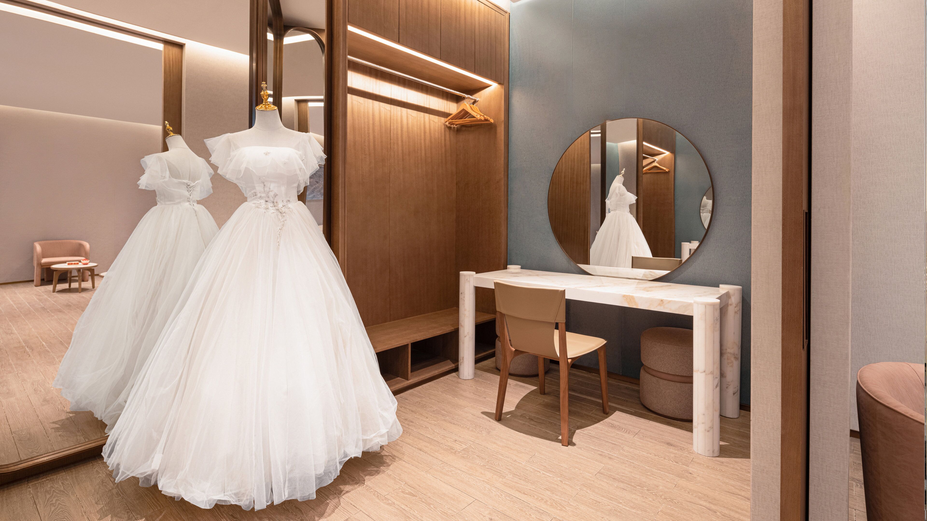 Uma boutique de noivas com espelho, mesa de toucador e dois vestidos em exposição.