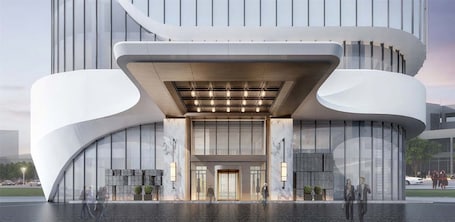 A modern building with a curved facade, large glass windows, and a prominent entrance with a light fixture above.