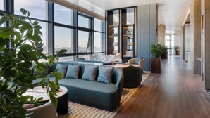 A modern living room with a sofa, coffee table, and a large window. There are bookshelves and a potted plant. - HUALUXE Qingdao Licang by IHG (Qingdao)