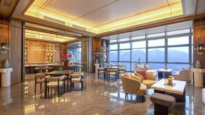 A spacious hotel lobby with a modern design, featuring a large seating area, a kitchen, and a view of the mountains through large windows. - HUALUXE Qingdao Licang by IHG (Qingdao)