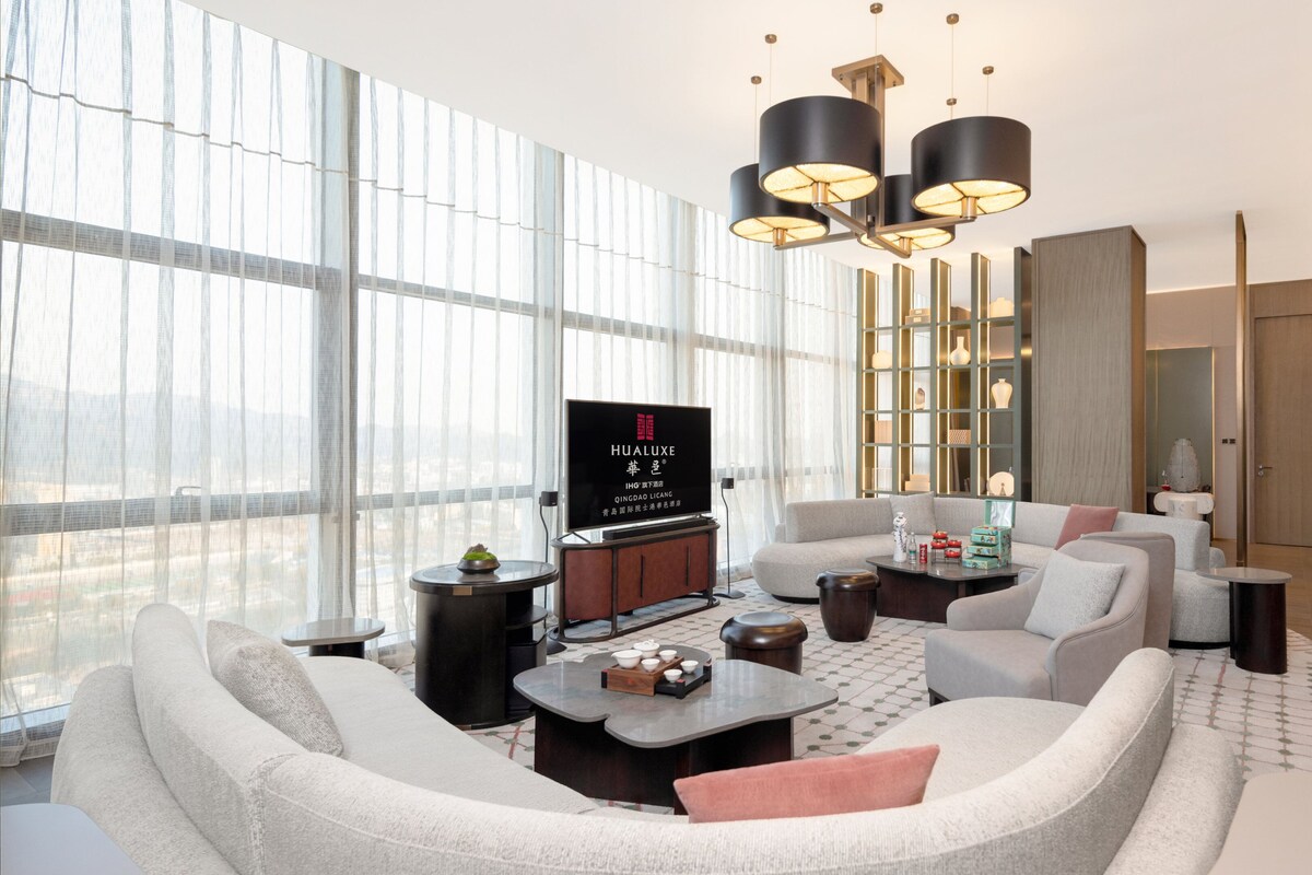 A modern living room with a large TV, comfortable seating, and a city view.