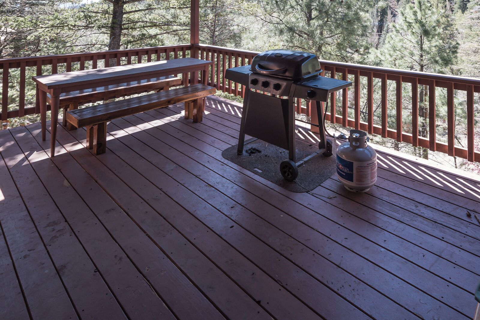 Een houten terras met een barbecue en een propaantank.
