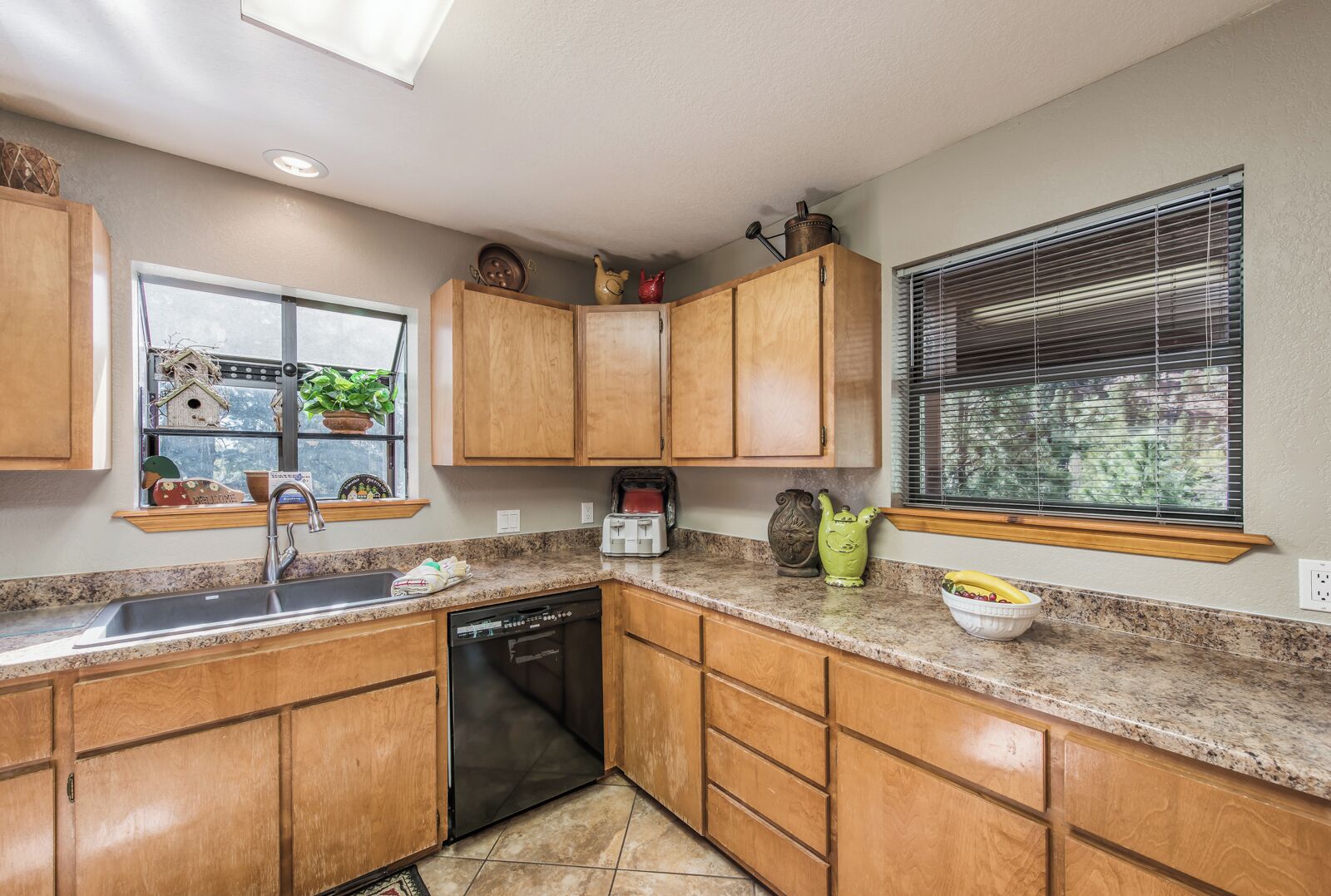 A kitchen with wooden cabinets, a dishwasher, a window with a view, and a countertop with a toaster and a bowl of fruit.