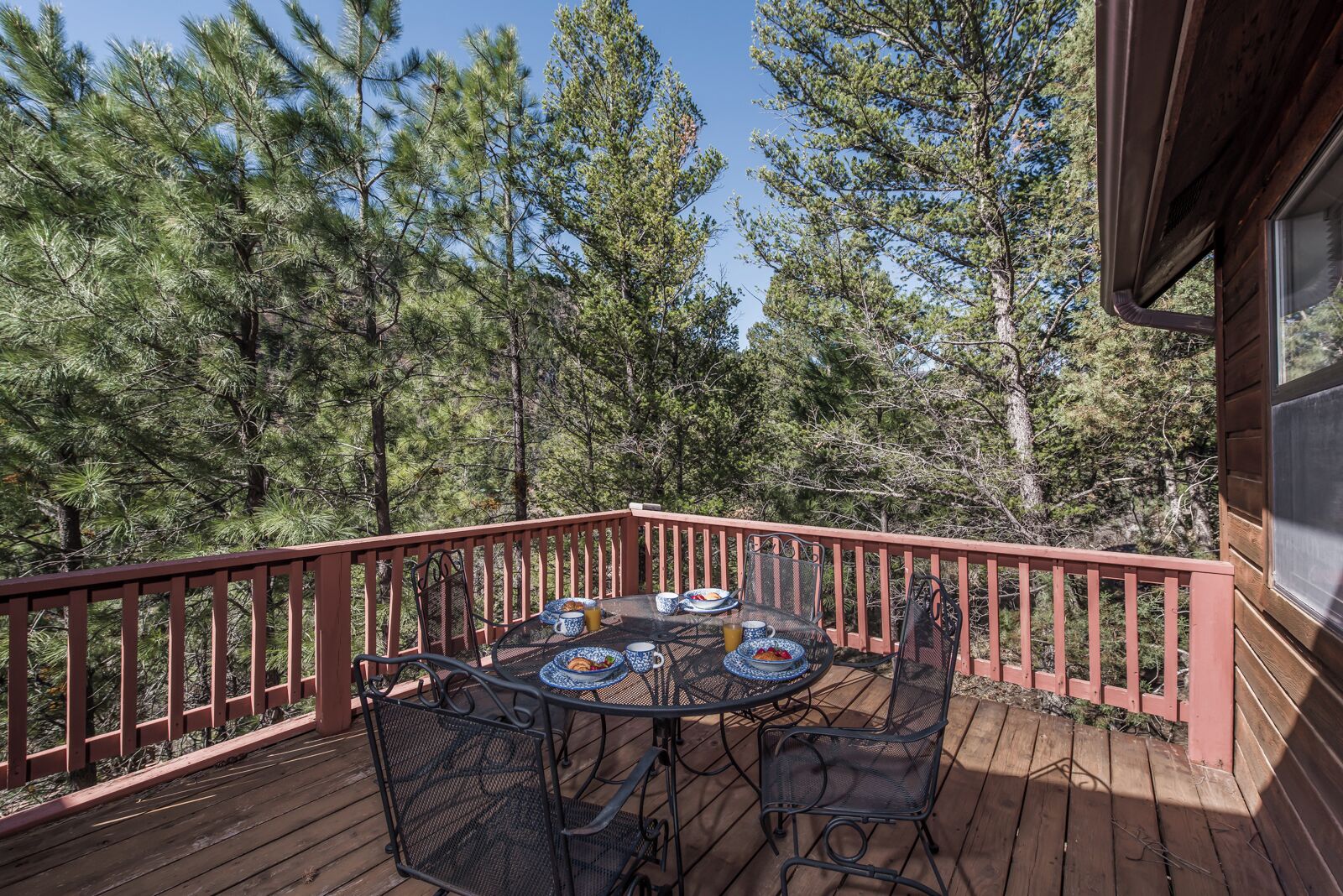 A wooden deck with a red railing, surrounded by tall pine trees.
