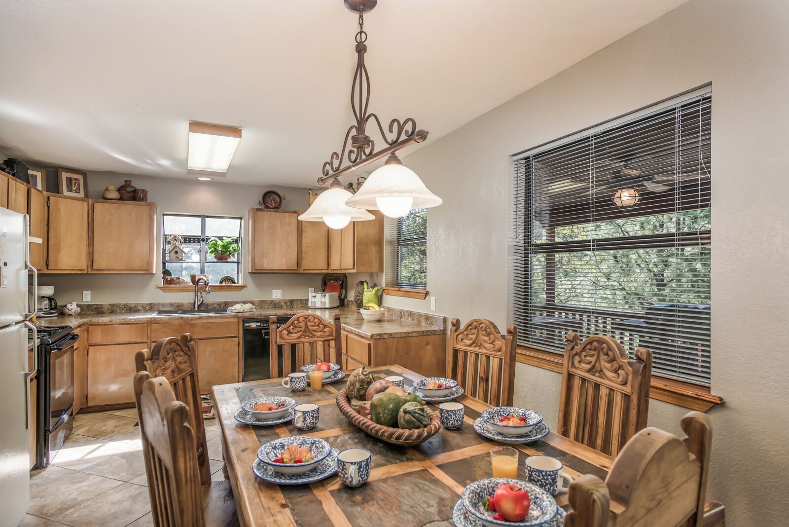 Une cuisine avec des meubles de rangement en bois, une table à manger dressée avec des assiettes et des tasses, et une fenêtre avec des stores.