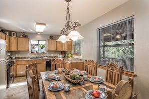 A kitchen with wooden cabinets, a dining table set with plates and cups, and a window with blinds. - Riverside House by Ruidoso Vacation Rentals (Ruidoso)