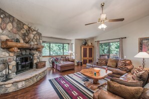 A spacious living room with a stone fireplace, leather furniture, and large windows offering a view of the outdoors.