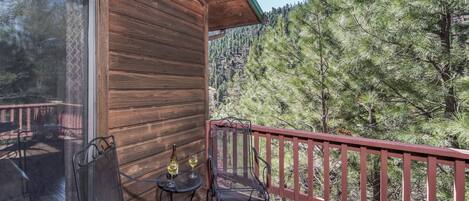 A wooden cabin with a balcony featuring two metal chairs and a small table with wine glasses.
