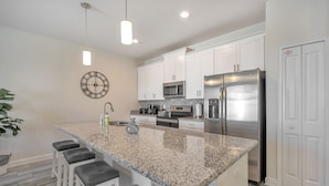A modern kitchen with granite countertops, stainless steel appliances, and a clock on the wall.