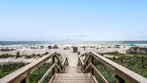 Un escalier en bois menant à une plage où se trouvent des parasols et des gens.