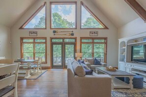 Un salón amplio con techo alto, ventanas grandes, chimenea y televisor.