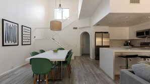 Et moderne køkken med hvide skabe, en central ø og et spiseområde med et hvidt bord og grønne stole.