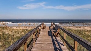 Un paseo marítimo de madera que conduce a una playa con un banco y una mesa.