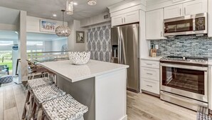 Una cocina moderna con una isla central, electrodomésticos de acero inoxidable y un salpicadero de baldosas en patrón de espiga.