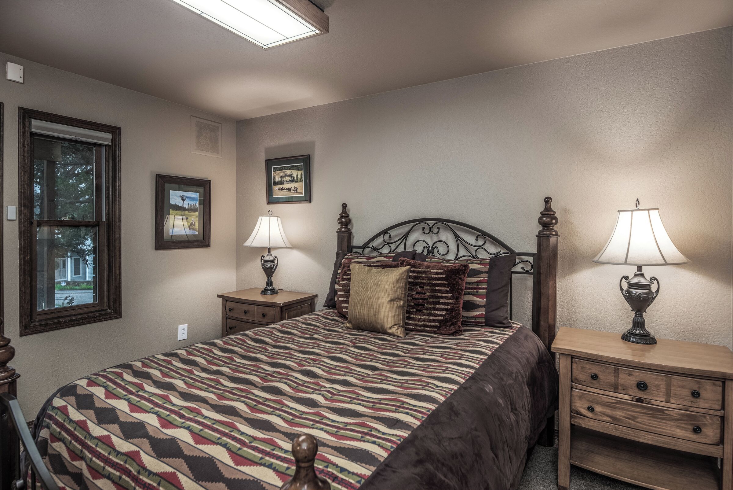 A bedroom with a large bed, two bedside tables with lamps, a window, and a framed picture on the wall.