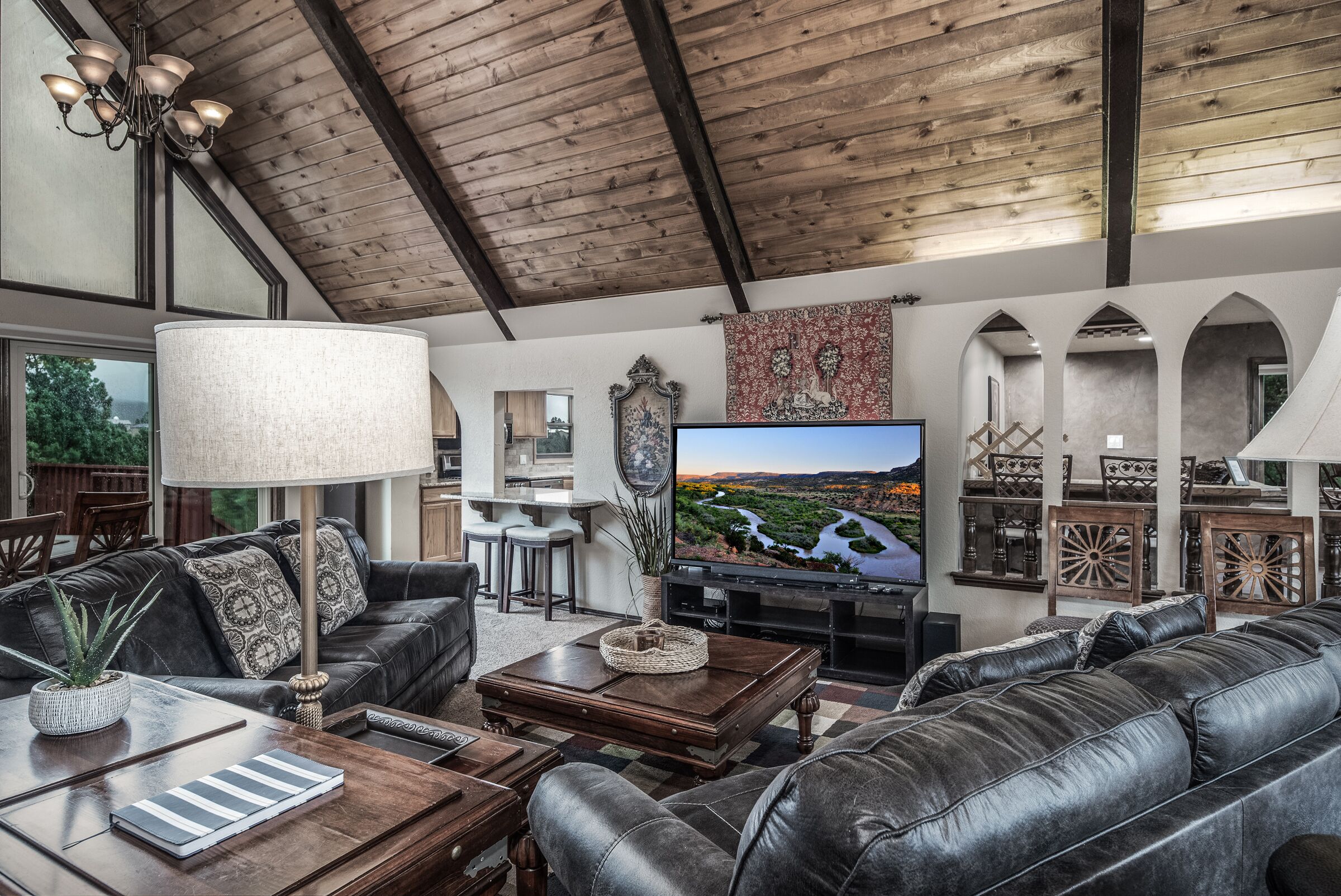 A spacious living room with a large TV, leather sofas, a wooden coffee table, and a chandelier.