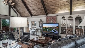 A spacious living room with a large TV, leather sofas, a wooden coffee table, and a chandelier. - White Mountain Chateau by Ruidoso Vacation Rentals (Ruidoso)