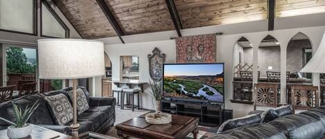 A spacious living room with a large TV, leather sofas, a wooden coffee table, and a chandelier.