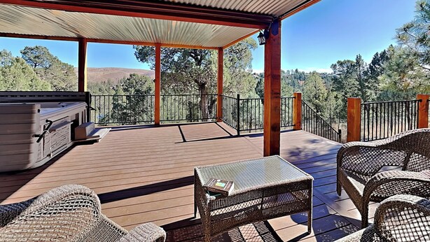 A covered outdoor deck with wicker furniture, a grill, and a view of trees and hills. - White Mountain Chateau by Ruidoso Vacation Rentals (Ruidoso)