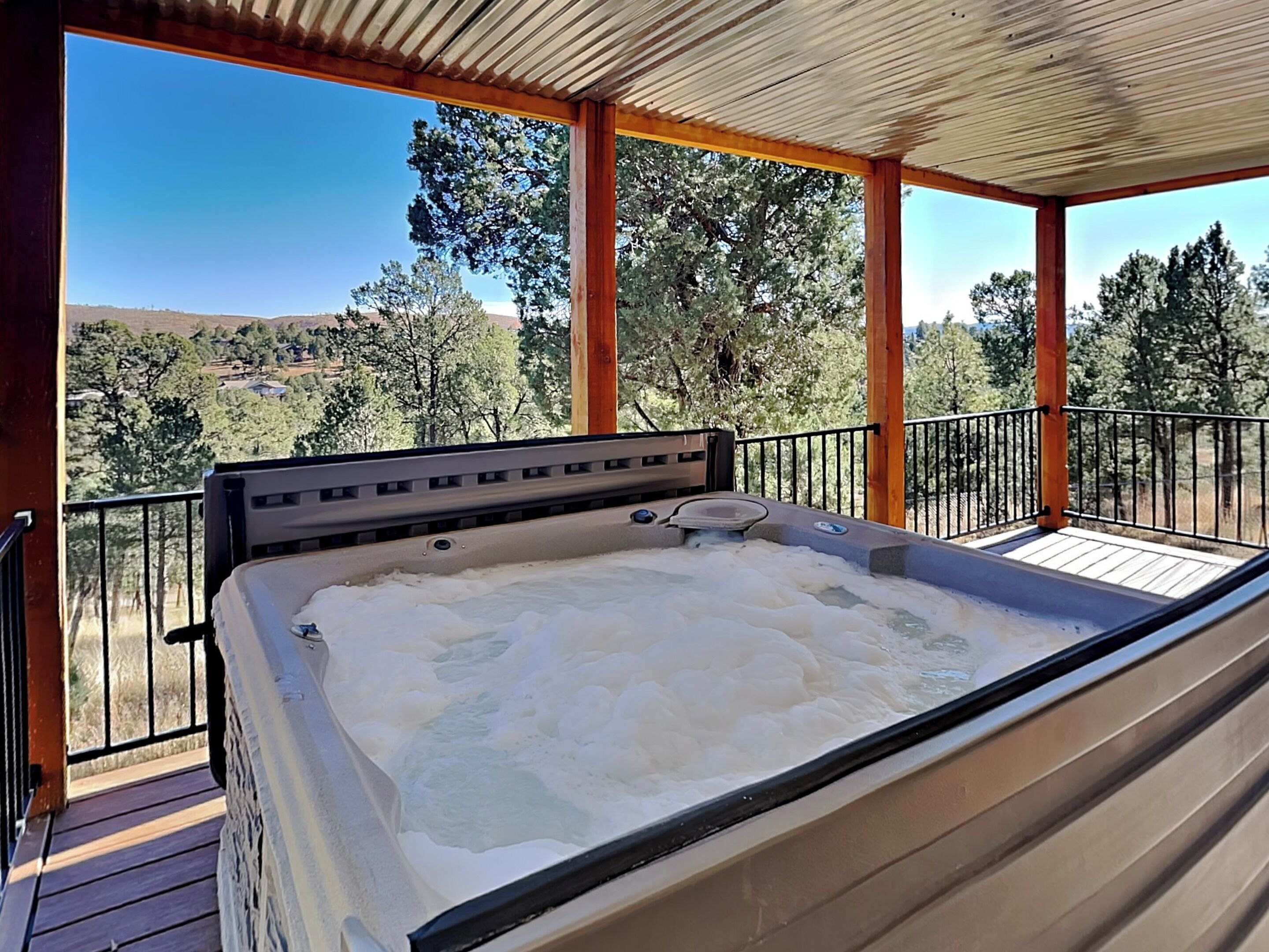 Ein Whirlpool auf einer Holzterrasse mit Blick auf Bäume und Hügel.