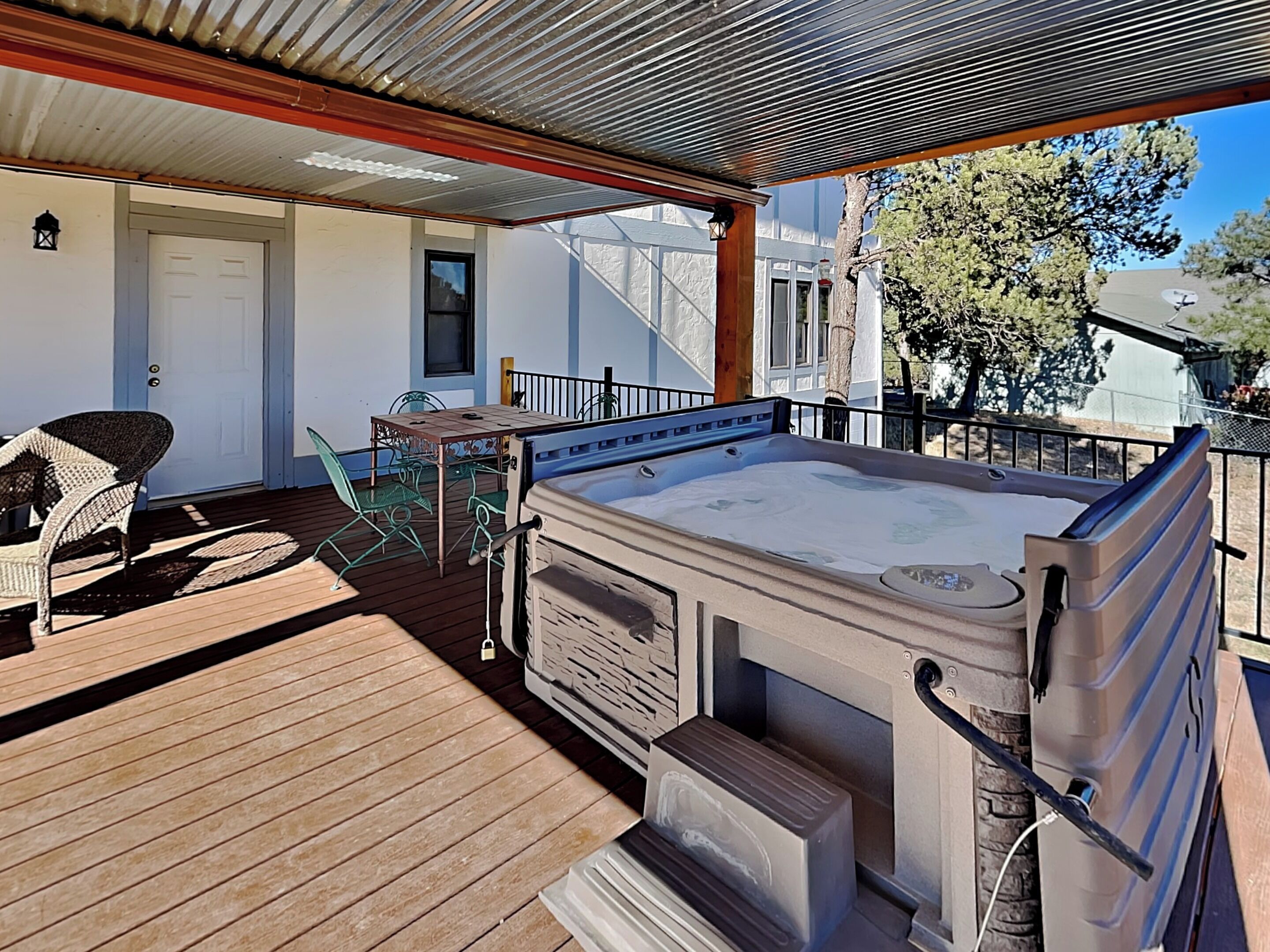 A wooden deck with a hot tub, outdoor furniture, and a covered area with a railing.