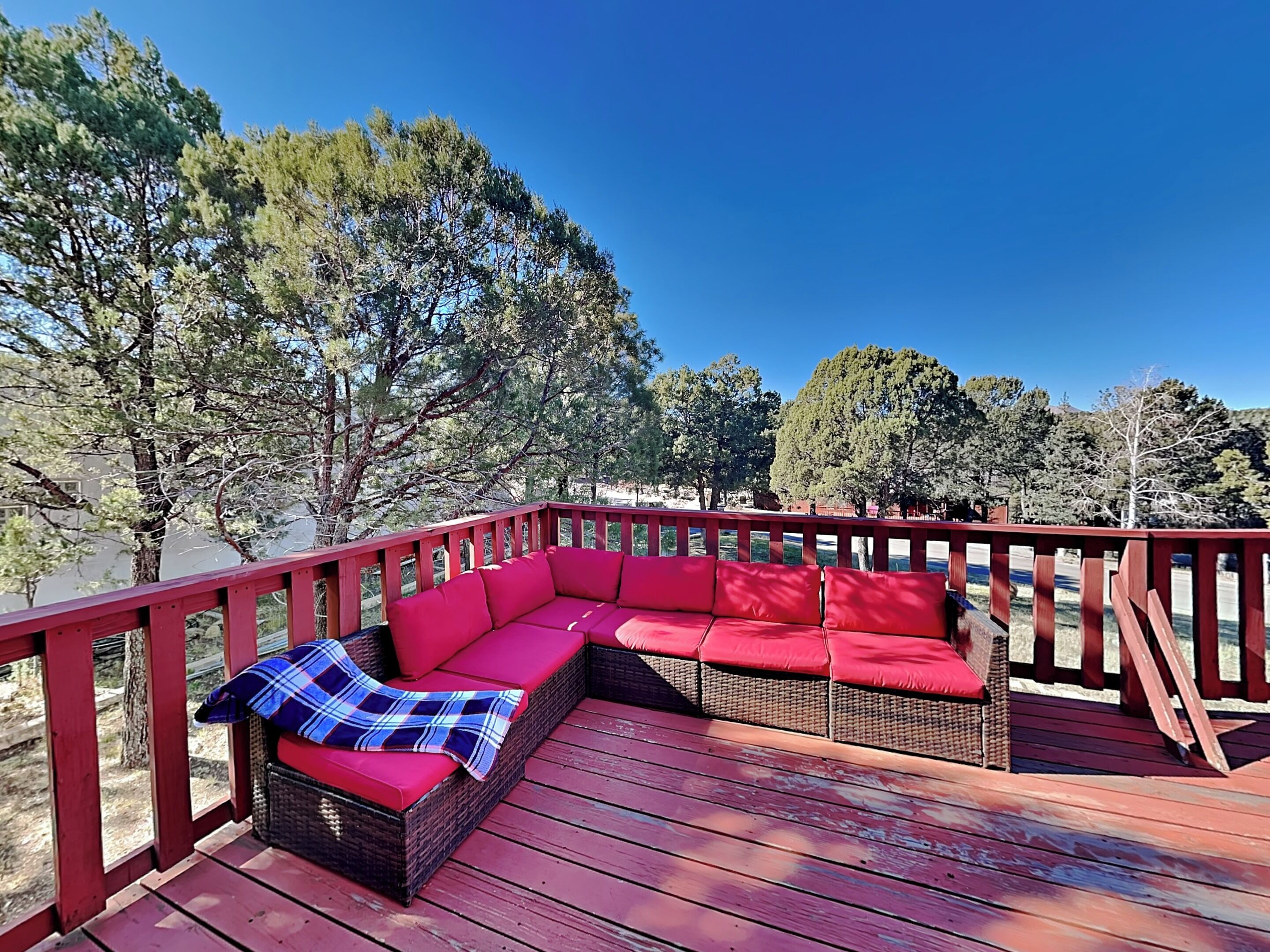 Eine Holzterrasse mit roter Geländer und einem roten, modularen Sofa mit Kissen.