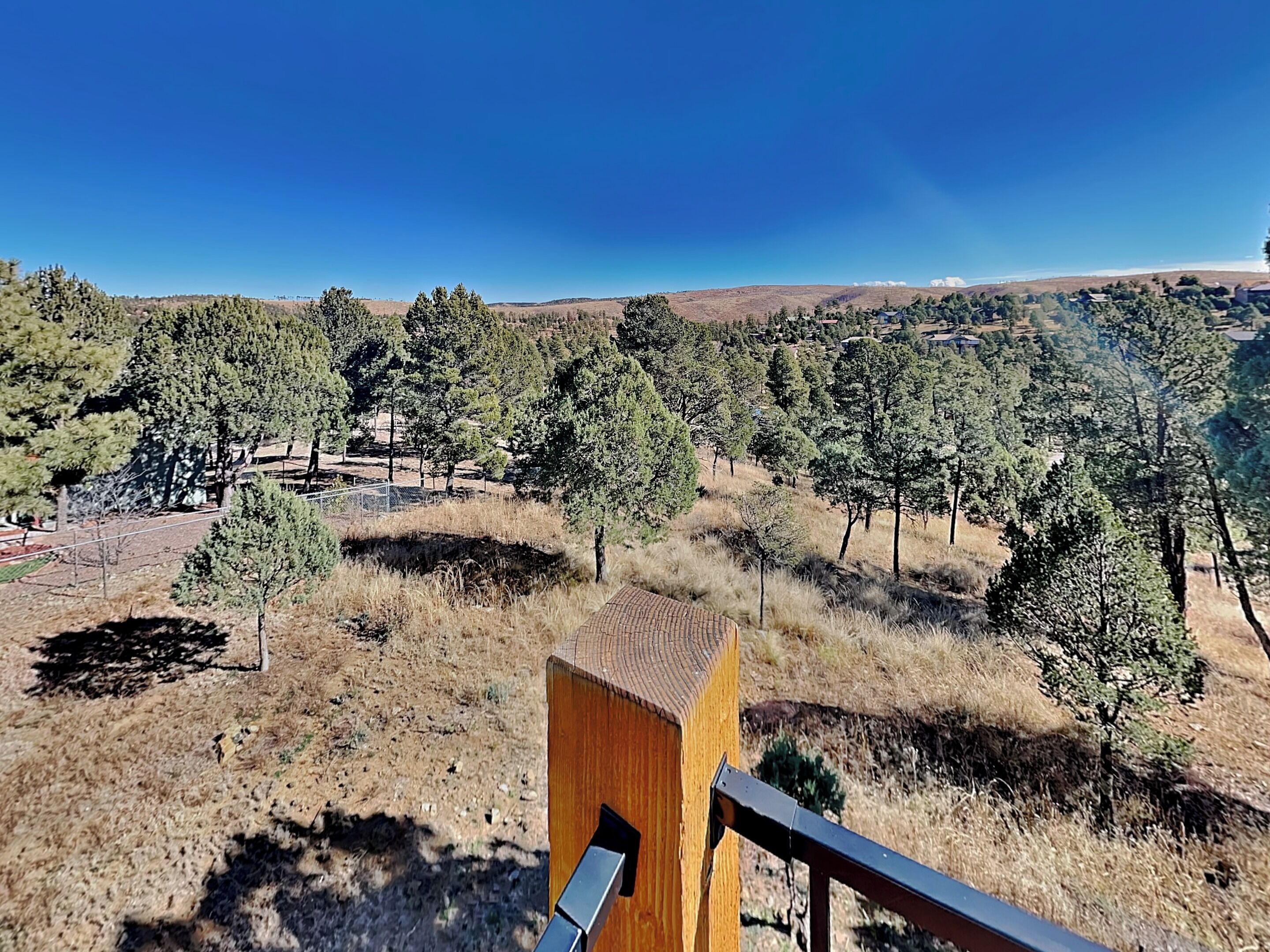 A view from a wooden balcony overlooking a dry, grassy landscape with scattered trees and distant hills.